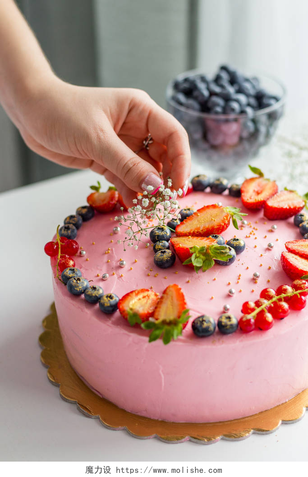 桌上的蛋糕和一碗蓝莓装饰美味蛋糕的女人 自制的粉色生日蛋糕，装饰有草莓、蓝莓、红醋栗和鲜花。 食物概念。 女孩生日或婚纱乳酪粉蛋糕